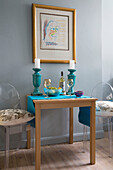 Geisterstühle am Tisch mit türkisfarbenen Kerzenhaltern und gerahmten Kunstwerken in einer Londoner Küche, England, UK