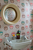 Konvexer Spiegel über dem Waschbecken mit gemusterter Weinetikettentapete in einem Haus in Surrey, England, UK