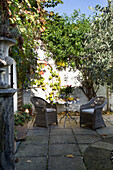 Wicker armchairs in sunlit paved courtyard of Berkshire garden,  England,  UK
