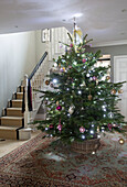 Großer Weihnachtsbaum auf gemustertem Teppich im Flur eines Hauses in Chobham, Surrey, England, Vereinigtes Königreich
