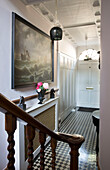Polished wooden banister with framed artwork above radiator cover in chequered hallway of London townhouse   England   UK