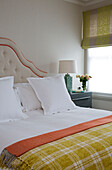 Checked yellow blanket on double bed with buttoned headboard at window in London home, England, UK