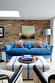 Books on ottoman with blue two-seater sofa in exposed brick living room of London home, England, UK