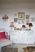 Botanical prints above white sideboard with pink cushion on chair in Norfolk home England UK