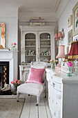 Rosa Kissen auf gepolstertem Stuhl mit Glasvitrine in einem Haus in Norfolk, England UK