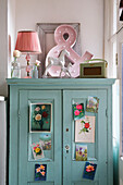 Pink lamp and ampersand on blue cupboard with botanical postcards in Norfolk home England UK