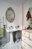 Decorative mirror above pedestal washbasin with chest of drawers in Norfolk home England UK