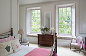 Wooden chest of drawers between bedroom windows in Sussex country house England UK