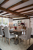 Upholstered dining chairs at candlelit table in beamed Surrey dining room England UK