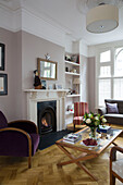 Purple armchair at fireside with low coffee table in living room of Victorian family home in South West London UK