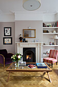 Armchairs and coffee table with lit fire in living room of Victorian family home in South West London UK