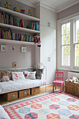 Book shelves above daybed with small pink chair in girls room of South West London family home UK