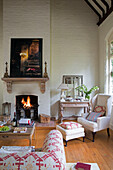 Armchair and footstool with lit fire in double height living room of renovated Victorian schoolhouse West Sussex England UK