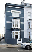 Car parked in front of blue and white three-storey terraced house on London street corner UK