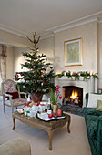 Christmas tree at fireside with gifts on ottoman in Sussex home England UK