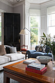Lilies and books on wooden coffee table with back door in living room of London townhouse UK