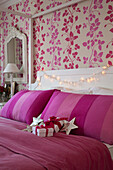 Weihnachtsgeschenke auf hellrosa Decke auf Himmelbett mit Blumentapete in einem Haus in Süd-London, England