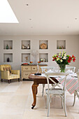 Wooden dining table in spacious room with skylight and alcove shelving Gloucestershire home England UK