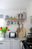 Cups hang on kitchen shelf above chopping boards and toaster in Worcestershire home England UK
