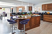 Purple leather bar stools at wooden kitchen island in open plan Sussex home England UK