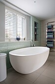 Freestanding bath under window with Venetian blinds and wall mounted towel rack in Sussex home England UK