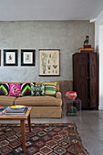 Dunkler Holzschrank mit botanischem Druck und Couchtisch mit hellen Streukissen auf Sofa in Londoner Wohnzimmer England UK
