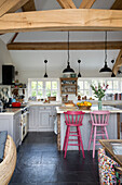 Painted pink bar stools in open plan beamed Sussex kitchen England UK