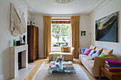 Art installation above fireplace with low glass coffee table and beige sofas in London townhouse living room England UK