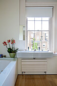 Weißes Waschbecken unter Schiebefenster mit Orchidee im Badezimmer eines Londoner Stadthauses England UK