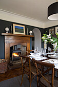 Befeuerter Kaminofen im Esszimmer mit Holztisch und Stühlen in einem Haus in Gloucestershire England UK