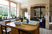 Wooden kitchen island with dark blue range oven view to adjoining room in Gloucestershire farmhouse England UK