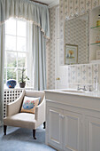 Light blue curtains with pelmet and chair beside washbasin with mirrored cabinet in Gloucestershire farmhouse England UK