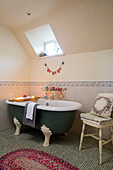 Freestanding bath below dormer window in mosaic tiled bathroom in Hampshire farmhouse England UK