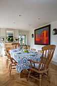 Wooden chairs at dining table with blue and white tablecloth in Gloucestershire cottage UK