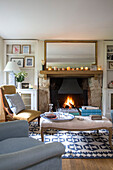 Gilt framed mirror and tealights above fire with ottoman in Gloucestershire cottage UK