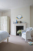 Korbstuhl am Kamin mit Kleiderschrank in einem Schlafzimmer mit Teppichboden in einem Londoner Stadthaus UK