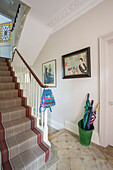 Umbrellas and schoolbag in hallway with brown carpeted staircase in London townhouse UK