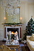 Crystal drop chandelier above coffee table with lit fire and Christmas tree in Kent country house England UK