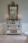 Lit candles and decorative mirror with shelving unit in bathroom of Kent country home England UK
