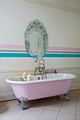 Rosa freistehende Badewanne mit Vintage-Spiegel und Wandstreifen in einem Landhaus in Kent, England, UK