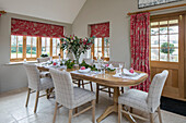 Checked dining chairs at table with red blinds and door curtain in Dorset farmhouse UK