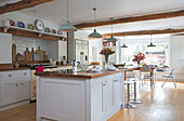 Pendant lights hang above white island unit in open plan kitchen of Oast house conversion Kent UK