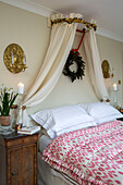 Cream bed canopy with gilt wall sconce and pink quilt in London townhouse UK