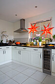 Zwei Leuchtsterne mit Dunstabzugshaube über dem Kochfeld in weißer Einbauküche eines Londoner Stadthauses UK