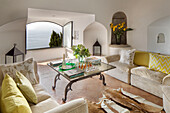 Gelbe Kissen auf cremefarbenen Sofas mit gläsernem Couchtisch und Blick auf das Meer in einer Villa an der Küste von Amalfi, Italien