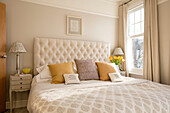 Yellow cushions on cream double bed at window of London home UK