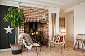 Wicker chairs and large houseplant et fireside in entrance hall of West Sussex farmhouse UK