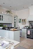 Light green fitted open plan kitchen with place setting at table in West Sussex townhouse UK
