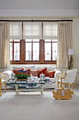 Geschnitzter Zeitschriftenständer mit weißem Sofa am Fenster und vergoldeten Stühlen in einem Stadthaus in West Sussex UK