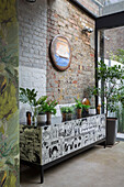Houseplants on pop art sideboard with exposed brick wall partly painted Victorian London townhouse UK